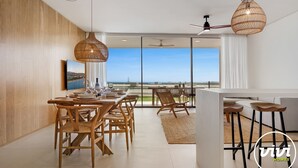 Un comedor moderno con vistas al mar, con muebles de madera y lámparas colgantes tejidas.