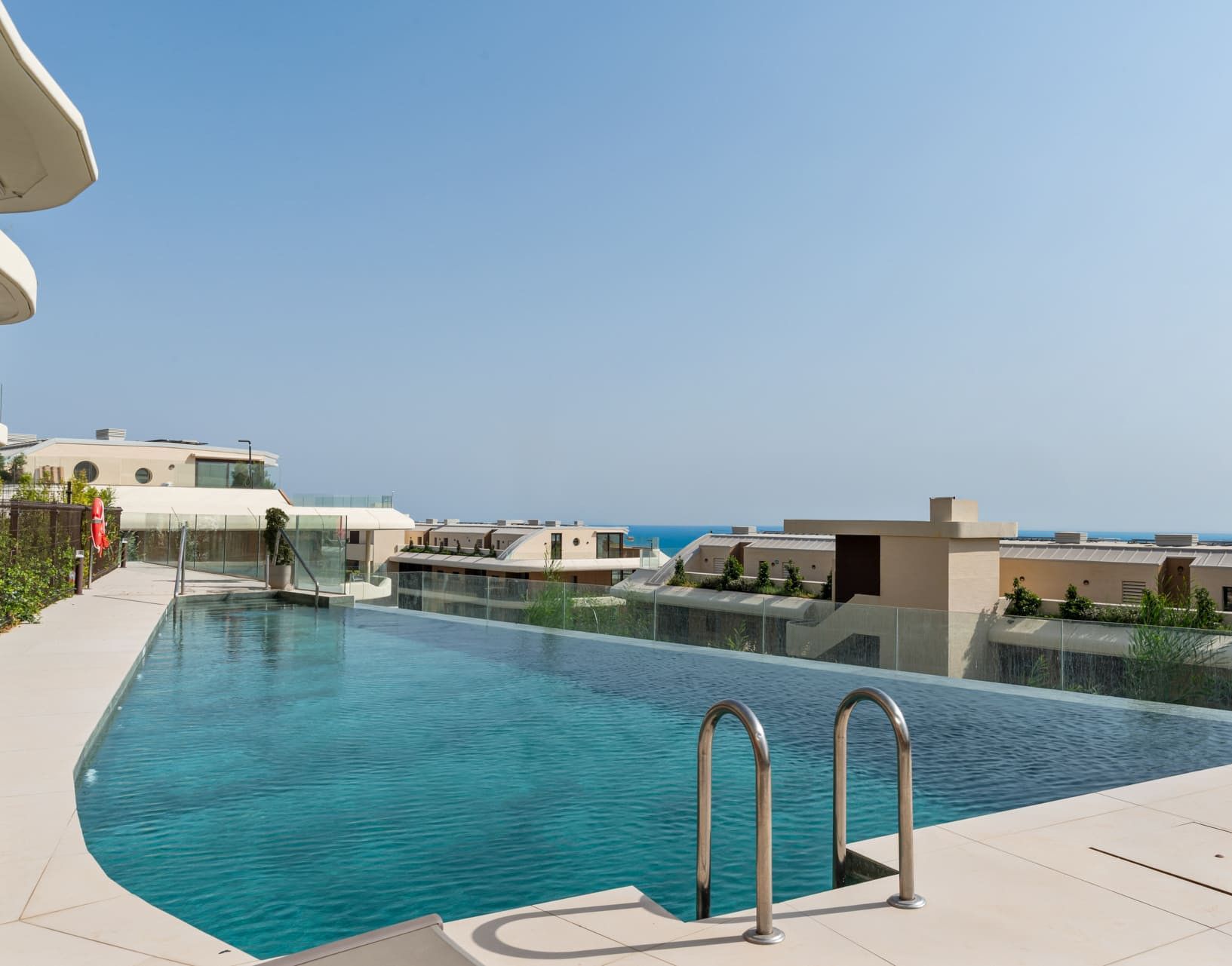 A modern swimming pool with clear blue water, surrounded by a tiled deck and glass barriers.