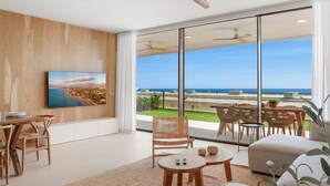 A modern living room with a large window overlooking a coastal view, a ceiling fan, and a dining area with wicker furniture. - Valley | Sea view - pool - terrace (Fuengirola)