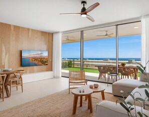 A modern living room with a large window overlooking a coastal view, a ceiling fan, and a dining area with wicker furniture. - Valley | Sea view - pool - terrace (Fuengirola)