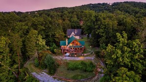 Eine große, mehrstöckige Blockhütte mit umlaufender Veranda, umgeben von dichtem Wald.