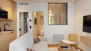 A modern living room with a sofa, a coffee table, and a TV. There is a kitchen area with a microwave and a sink. - Beautiful Apartment- Jardin de Luxembourg (Paris)