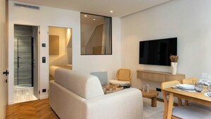 A modern living room with a sofa, a dining table set for two, and a television mounted on the wall. - Beautiful Apartment- Jardin de Luxembourg (Paris)