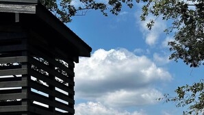 Une cabane en bois, dotée d’un toit en pente, entourée d’une végétation luxuriante et d’arbres, et offrant une vue sur un paysage vallonné.