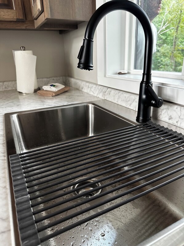 A stainless steel kitchen sink with a black faucet and a built-in strainer.