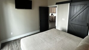 Une chambre avec un grand lit, un ventilateur de plafond, une porte sombre et une vue sur la cuisine.