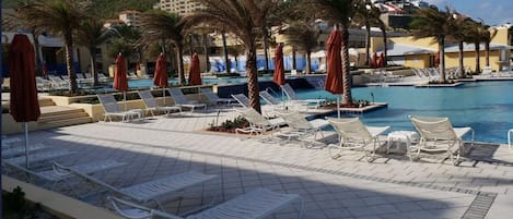 A poolside area with lounge chairs and umbrellas, a pool, and a hillside in the background.