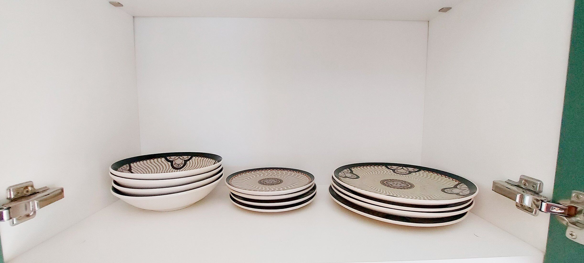 A white cabinet with three stacks of plates, each with a black rim and a decorative center.
