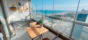 A balcony with a wooden table, chairs, and a potted plant. - COCAZ0102 - Smart Costa Azul (Salvador)