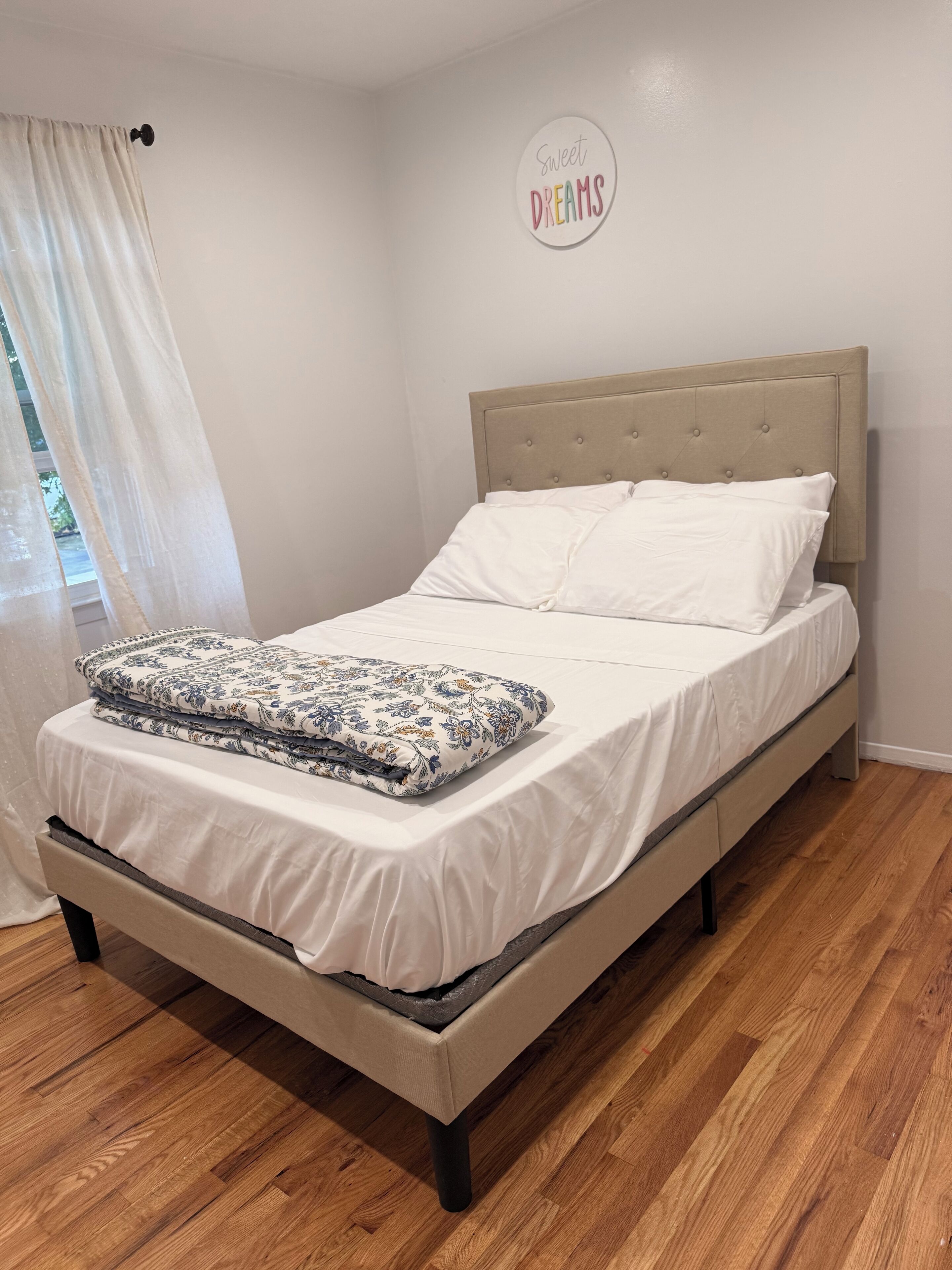 Una cama bien hecha con un cabecero color beige, ropa de cama blanca y una almohada con estampado floral.