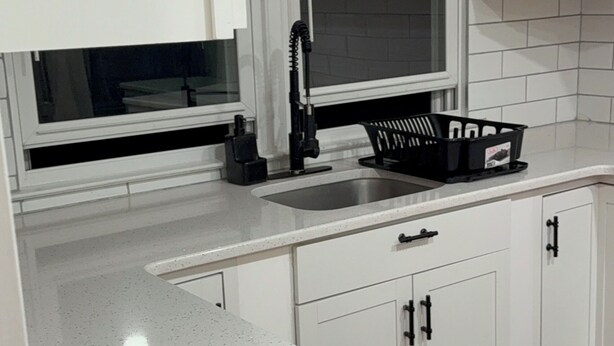 A kitchen with white cabinetry, a stainless steel sink, a black faucet, and a window with blinds.