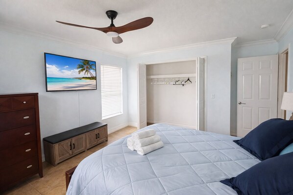 Une chambre à coucher comprenant un lit, un ventilateur de plafond, une commode, un tableau et un dressing.