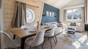 A modern living room with a dining area, wooden walls, a blue accent wall, and a large window with a mountain view. - 50m from resort center, 6th floor, view panoramic/resort, tv, 38m², Avoriaz (Avoriaz)