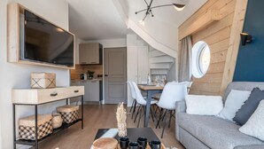 A modern living room with a grey sofa, a wooden coffee table, and a TV mounted on the wall. There is a dining area with white chairs and a table, and a kitchen in the background. - 50m from resort center, 6th floor, view panoramic/resort, tv, 38m², Avoriaz (Avoriaz)