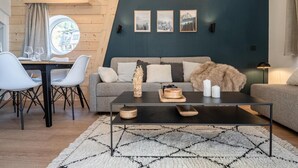A modern living room with a grey sofa, a round dining table with chairs, a coffee table with decorative items, and a large window with curtains. - 50m from resort center, 6th floor, view panoramic/resort, tv, 38m², Avoriaz (Avoriaz)