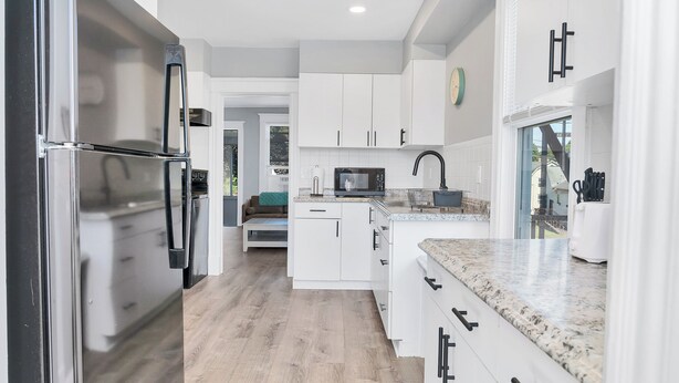 Una cocina moderna con muebles blancos, un refrigerador de acero inoxidable y una encimera de granito.
