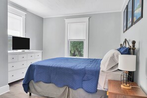 Ein Schlafzimmer mit einem Bett, einem Nachttisch mit Lampe, einer Kommode und einem Fernseher.