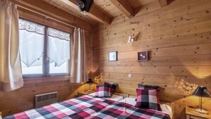 A cozy cabin room with a large bed, two bedside tables with lamps, wooden walls, and a window with curtains.