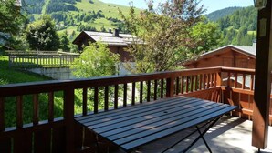 A wooden deck with a table and chairs, overlooking a mountainous landscape with houses.