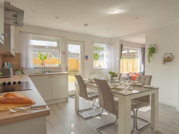 A modern kitchen with a dining area, large windows, and a view of the outdoors.