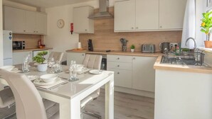 A modern kitchen with white cabinetry, a dining table set for four, and a small island with a sink. - Etive House - 3 bedroom stylish home (Condorrat)