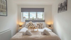 A bedroom with a bed, two bedside tables, a window, and a wall with a picture. - Etive House - 3 bedroom stylish home (Condorrat)