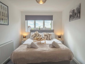 A bedroom with a bed, two bedside tables, a window, and a wall with a picture.