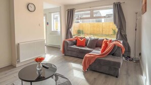 A living room with a sofa, a round table with a vase, and a window with curtains. - Etive House - 3 bedroom stylish home (Condorrat)
