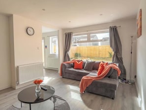 A living room with a sofa, a round table with a vase, and a window with curtains.