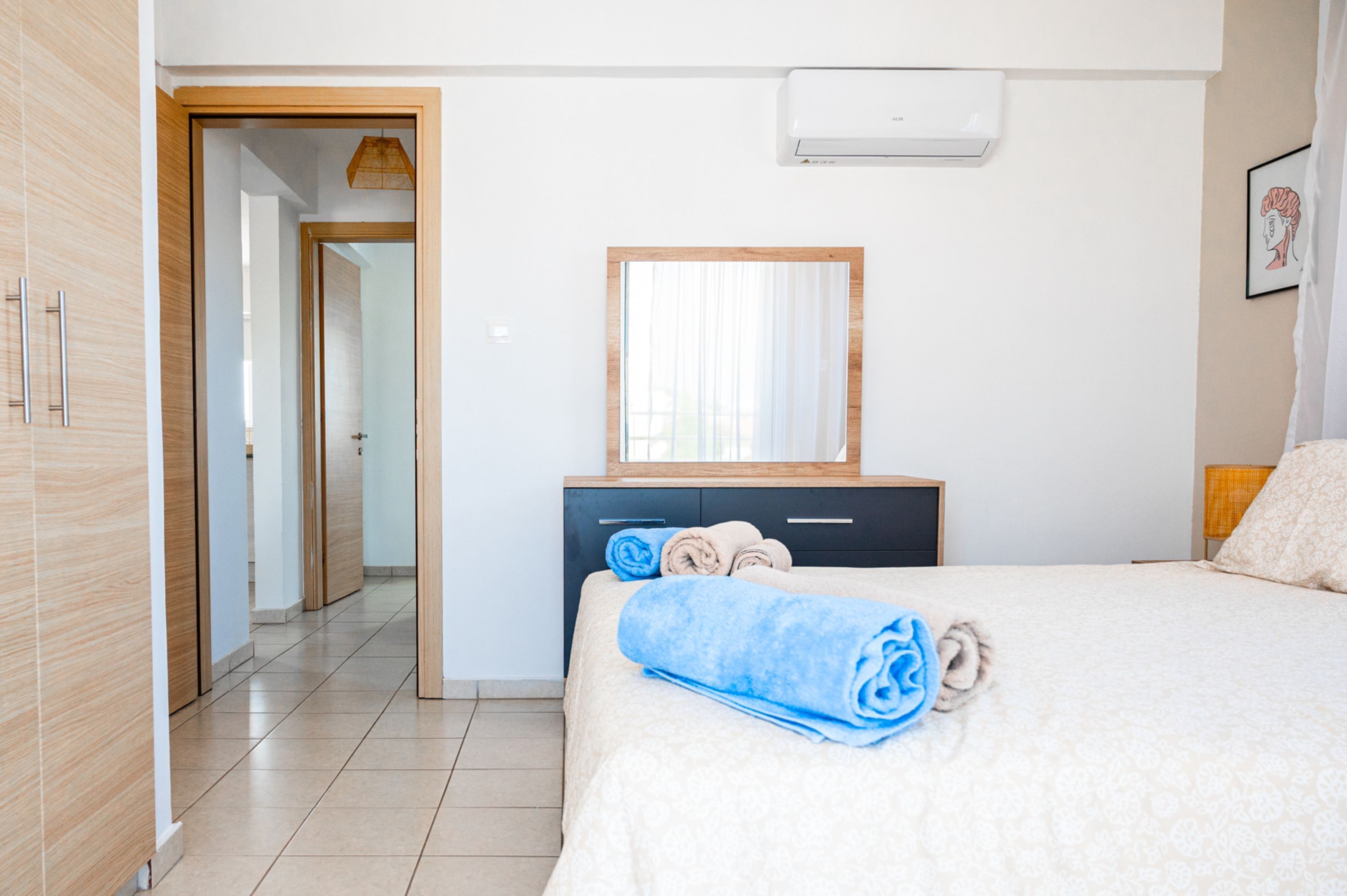 A hotel room with a bed, a wooden wardrobe, a mirror, and a window with curtains.