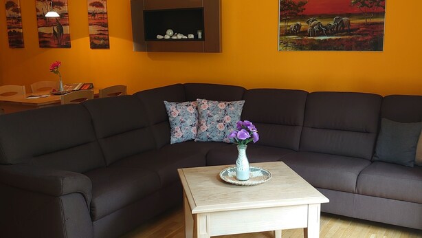 A living room with a dark brown sofa, a wooden coffee table, and a grey ottoman. There is a painting on the wall and a small shelf with decorative items. - Apartment at the Glubigsee (Wendisch Rietz)