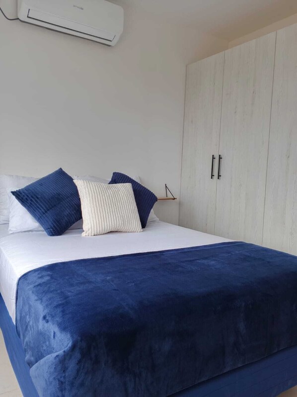 A bedroom with a bed, pillows, a wardrobe, and an air conditioning unit.