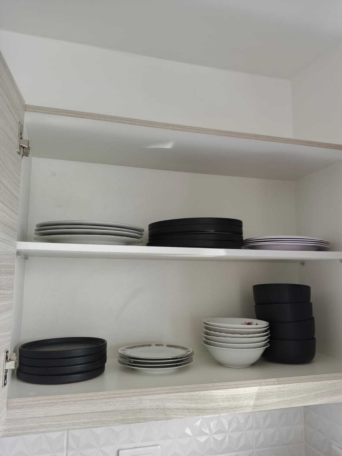 A kitchen cabinet with shelves holding stacked plates and bowls.