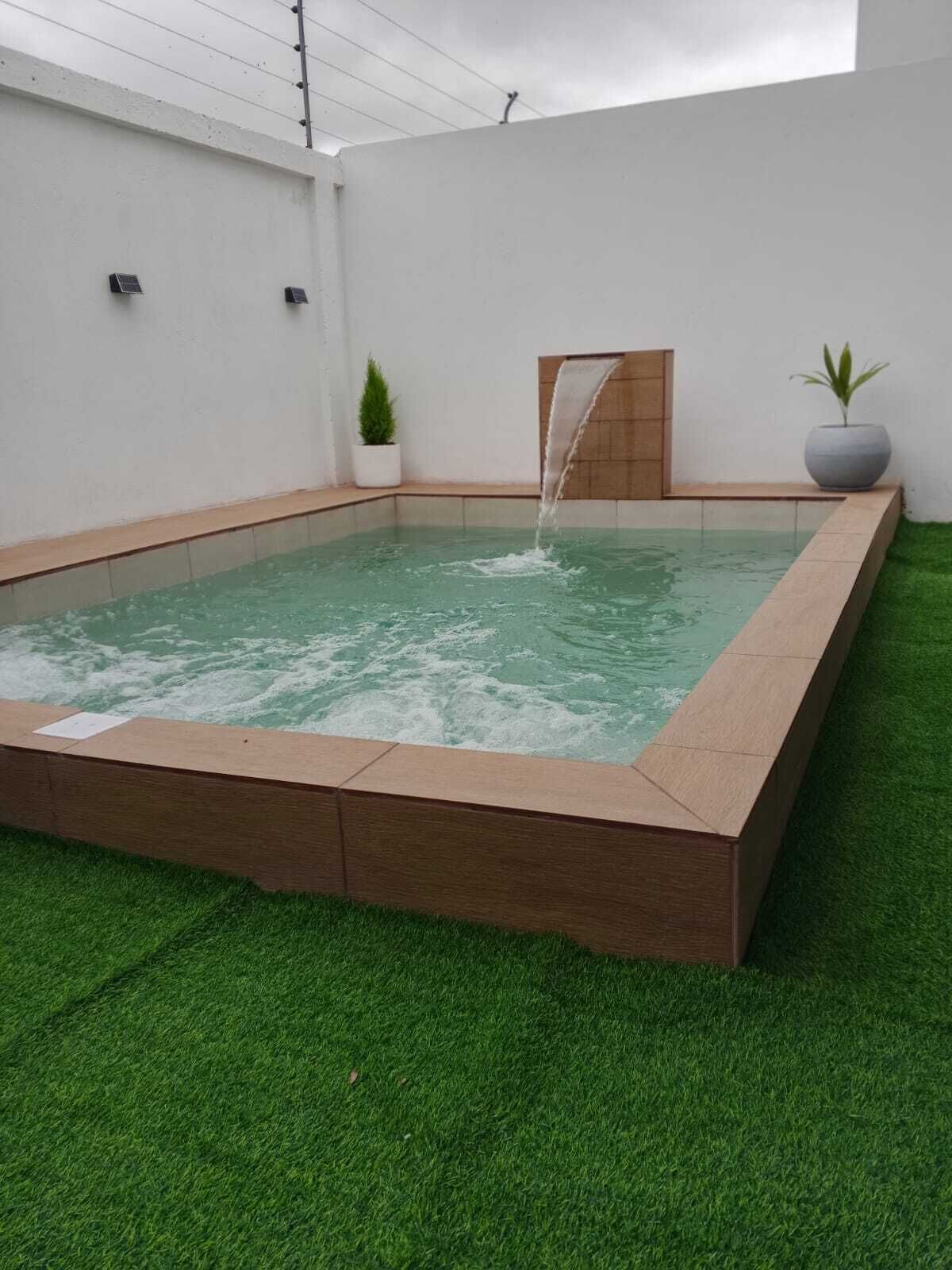 A rectangular hot tub with a waterfall feature, surrounded by artificial grass and white walls.