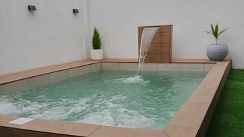A rectangular hot tub with a waterfall feature, surrounded by artificial grass and white walls.