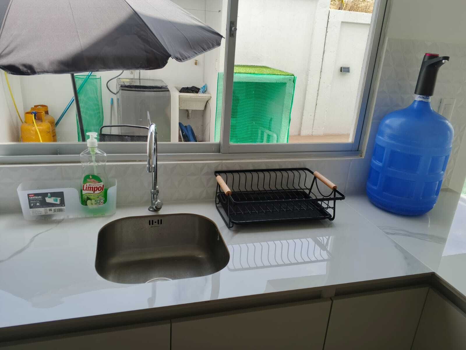 Una cucina con un lavello, una bottiglia di detersivo per piatti, una griglia metallica nera e un contenitore blu per l'acqua.