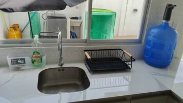Una cucina con un lavello, una bottiglia di detersivo per piatti, una griglia metallica nera e un contenitore blu per l'acqua.