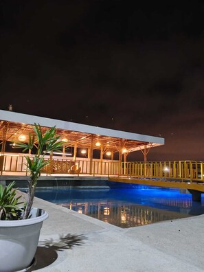 A nighttime view of a pool area with a covered seating area and a potted plant in the foreground.
