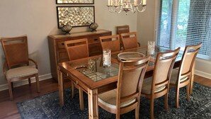 Ein Esszimmer mit einem Glastisch, Holzsesseln, einer Chandelierleuchtre und Bildern an der Wand.