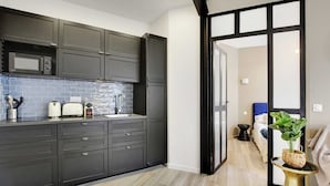 A modern kitchen with dark cabinets, a microwave, and a sink. There is a dining area with a table and chairs, and a plant on a side table. - Lovely Apartment - 1br/4p - Buttes-chaumont (Paris)
