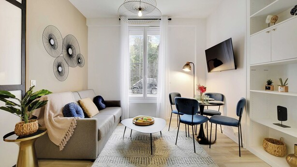 A modern living room with a sofa, coffee table, and chairs. There is a dining area with a table and chairs. A TV is mounted on the wall, and there are shelves with decorative items. - Lovely Apartment - 1br/4p - Buttes-chaumont (Paris)