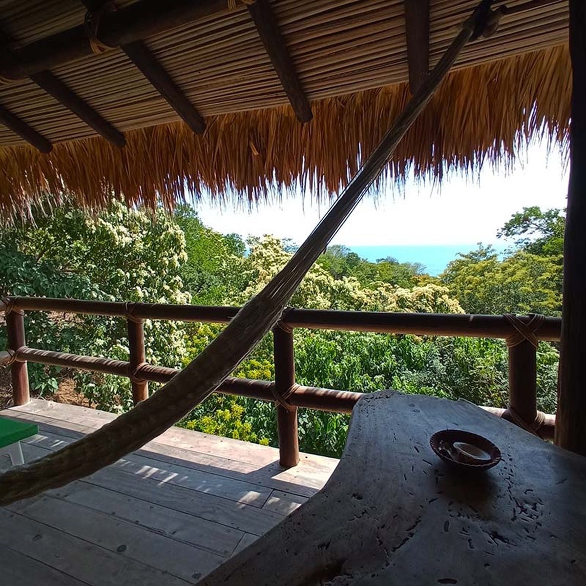 Una terraza de madera con techo de paja, con vistas a un paisaje exuberante y el mar.