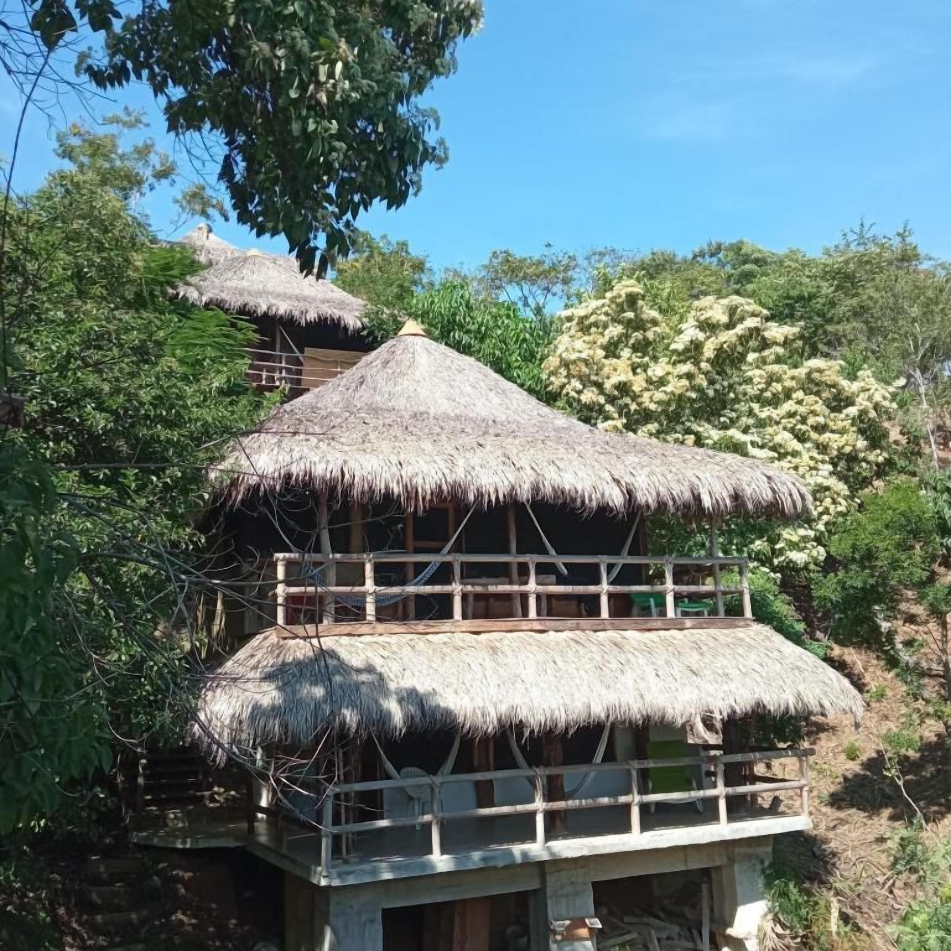 Um edifício de dois andares com telhado de palha, rodeado por vegetação.