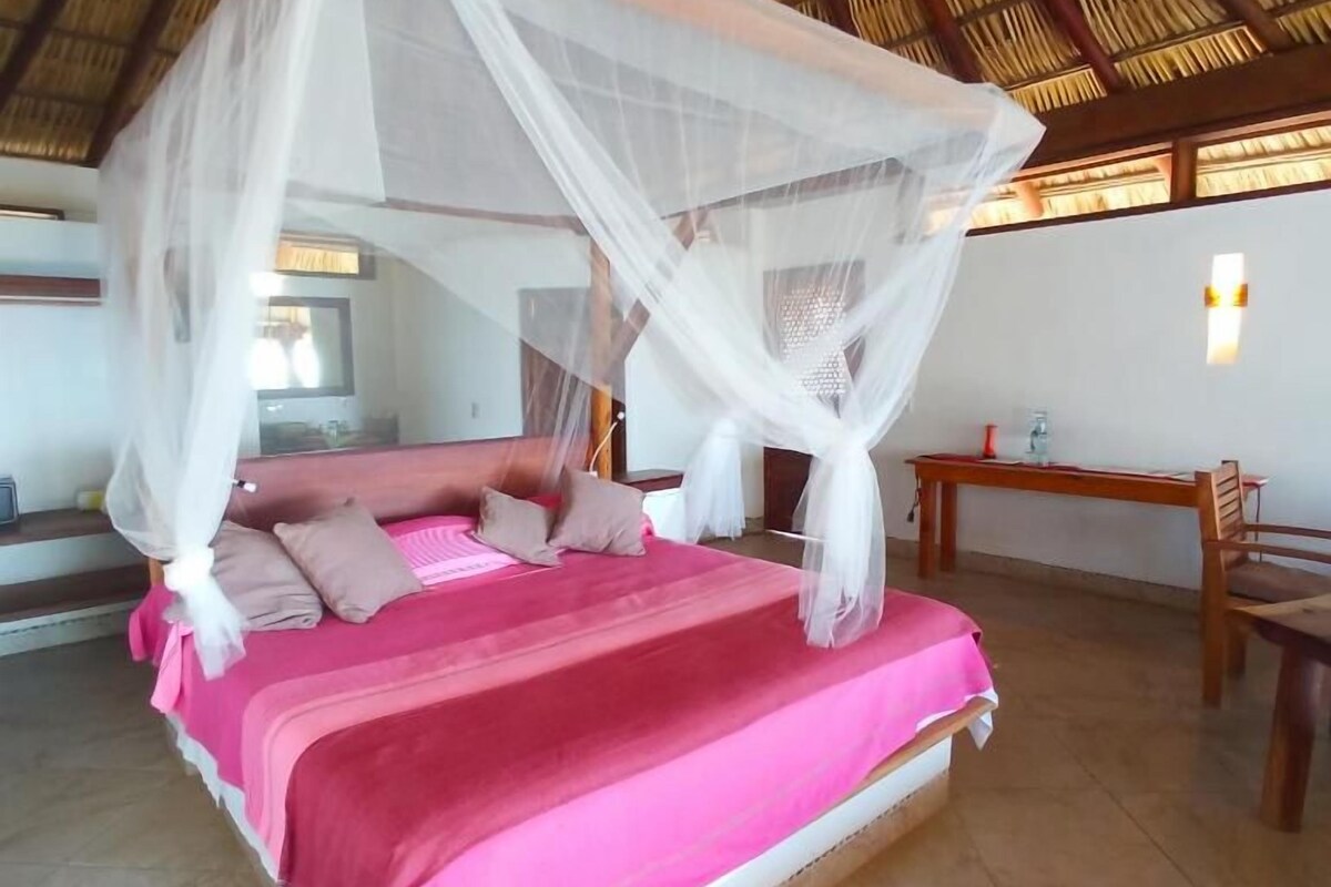 A bed with a canopy, a wooden table, and a chair in a room with a tiled floor.