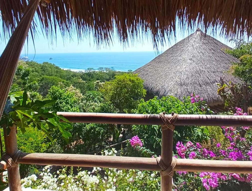 Una estructura con techo de paja rodeada de exuberante follaje y flores vibrantes, con vista al océano.