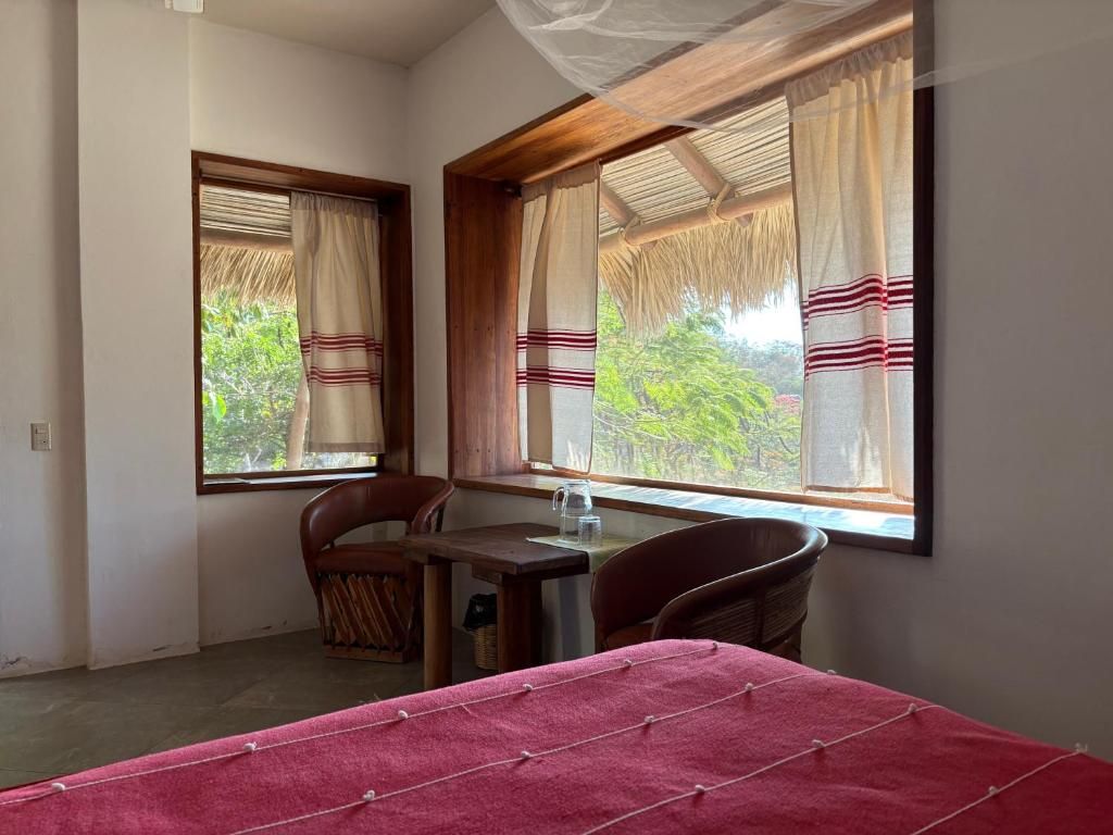 Una habitación con una cama, dos sillas, una mesita y un ventanal con cortinas.