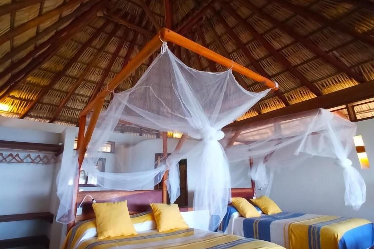 A room with a thatched roof, a bed with a canopy, and a second bed with a striped bedspread.