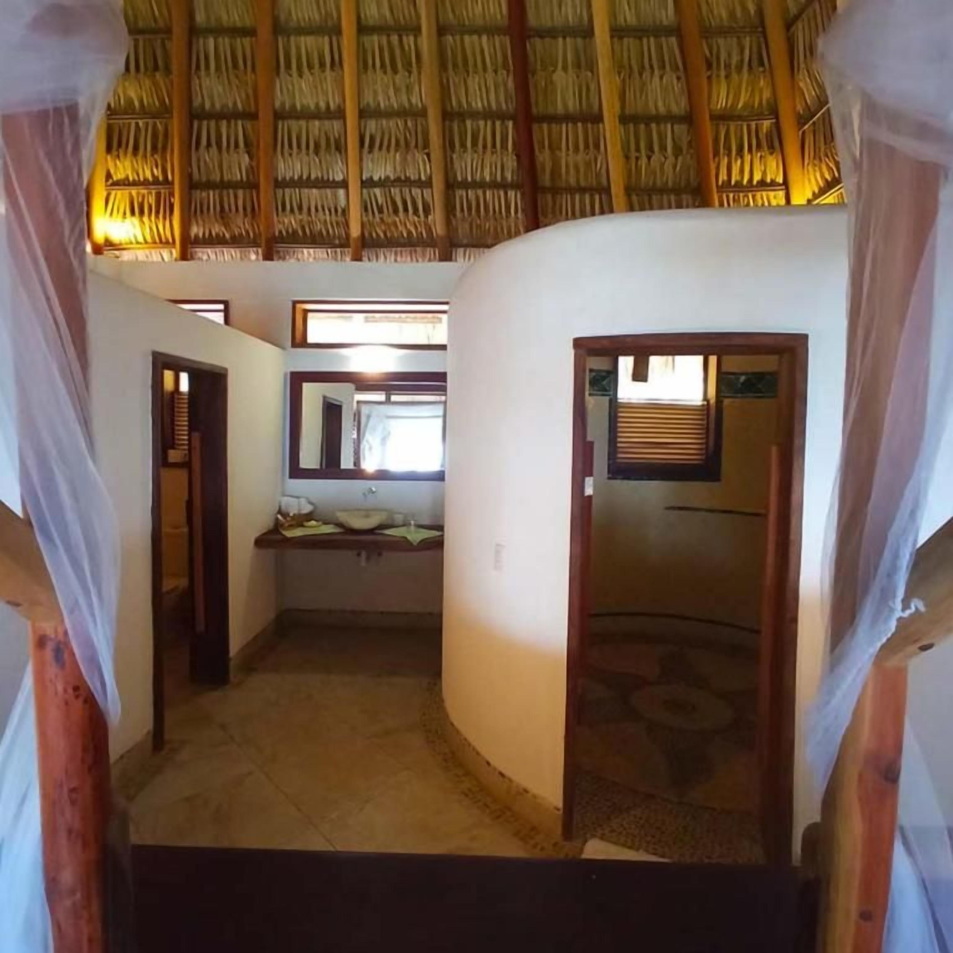 Una habitación con techo de paja, un ventanal pequeño y una puerta que da a otra estancia.