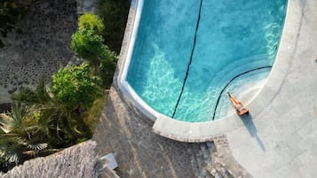 Vista aérea de uma piscina com água cristalina, rodeada por degraus de pedra e vegetação.