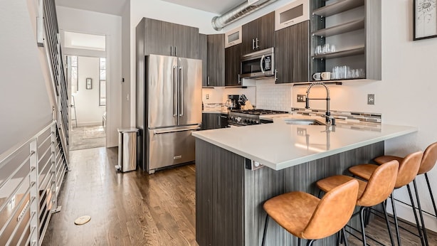 A modern kitchen with stainless steel appliances, a central island with bar stools, and a view of the adjacent living area.
